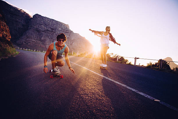 Friends longboard skating on road sunset Teenage Friends having fun longboard skating on mountain road sunset longboard skating photos stock pictures, royalty-free photos & images