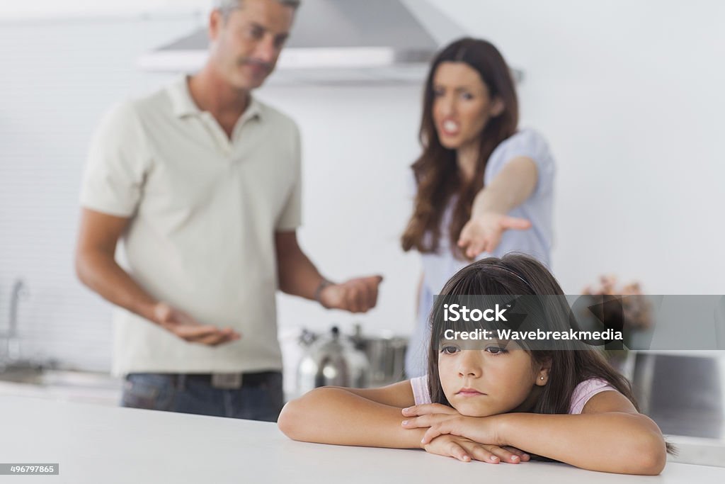 Couple having dispute in front of their upset daughter Couple having dispute in front of their upset daughter sitting in kitchen at home 30-39 Years Stock Photo