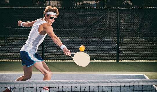 A retro 80's style guy playing pickleball on a court.