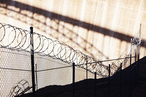 Razor wire barbed chain link fence barrier - with bridge shadow background.
