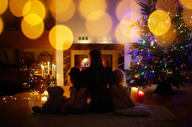 istock Young mother and daughters sitting by a fireplace on Christmas 496803528