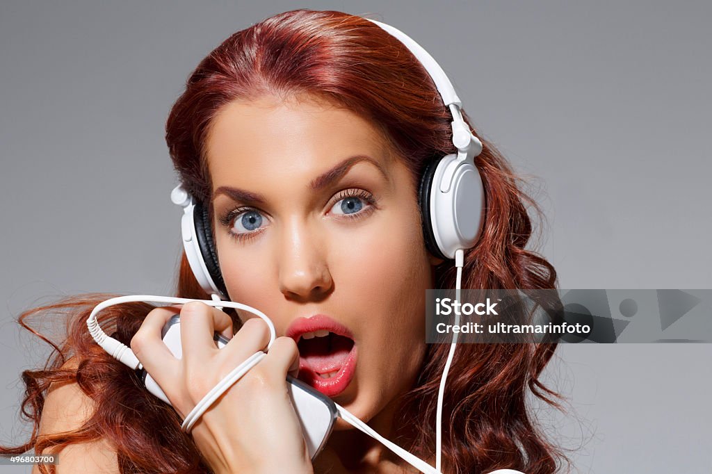 Music  Beauty Portrait    Young women listening to headphones  and singing Young women listening to headphones  and singing, music, using mobile phone. Beauty Portrait. Unique lifestyles. Original looks.  Red hair,  Blue Eyes.  Studio shot.  Developed from RAW, Adobe RGB color profile. 20-24 Years Stock Photo