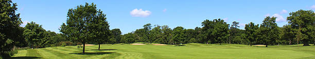 Wide panorama image of golf course, bunkers, trees, blue sky