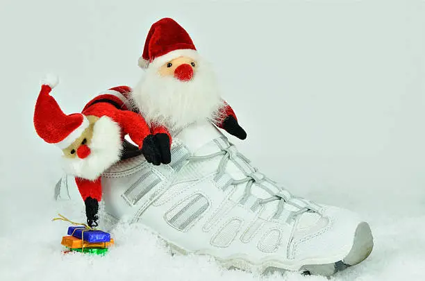 Santa Claus, twice, with sweets inside a white sports shoe on white, snowy background, close up, horizontal