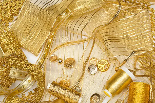 Close-up studio shot of golden sewing notions, ribbon, lace, threads and buttons.