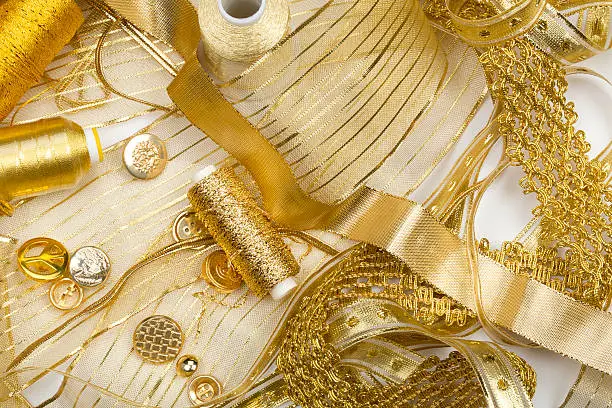 Close-up studio shot of golden sewing notions, ribbon, lace, threads and buttons.