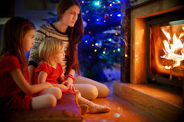istock Young mother and daughters sitting by a fireplace on Christmas 496828232