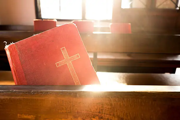 The old red books or red worship songbooks at wooden  bench in church  with soft sun light. Vintage Style.