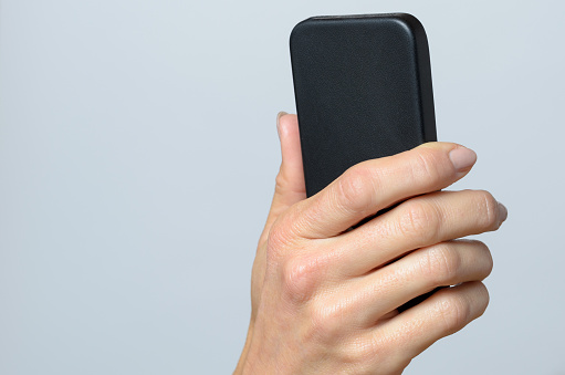 Hand holding a black cellular Against Gray Background with Copy Space.