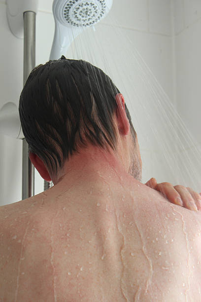 Young man taking a shower, washing his back and shoulders Photo showing a young man taking a shower, washing his back and shoulders under the water, and rinsing the shampoo from his dark brown hair. shower men falling water soap sud stock pictures, royalty-free photos & images