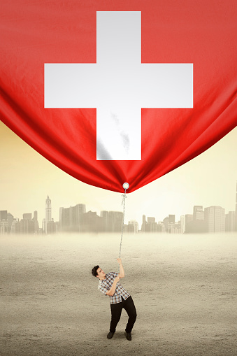 Image of young man with casual clothes drags flag of Switzerland, shot outdoors