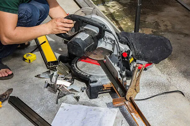 Worker cutting steel tube with sliding compound mitre saw.