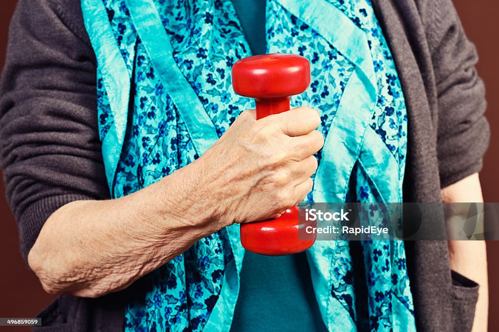 Senior fitness: elderly hand lifts dumbbell An elderly female hand lifts a bright red barbell. Keeping fit in old age is important! Active Lifestyle Stock Photo