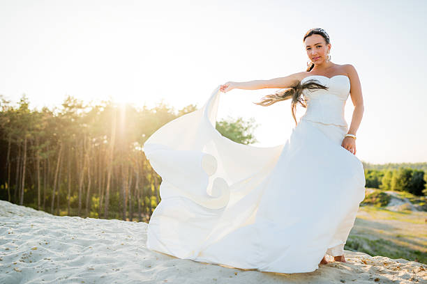 Beautiful bride stands on a cliff above the lake in a glamorous white wedding dress