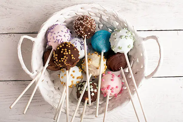 Batch of cake pops in the white basket on a wooden table