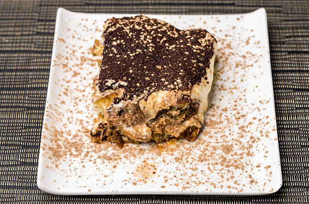 A pyramid of tiramisu desserts is captured in a cafe in Rome on an idyllic autumn day. The yellow and brown tiramisu desserts in transparent bowls look tasty. It is a close up of the food.
