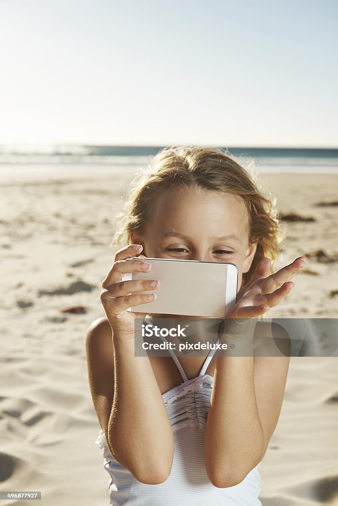 Little miss explorer Shot of an adorable little girl playing with a phone on the beach Beach Stock Photo