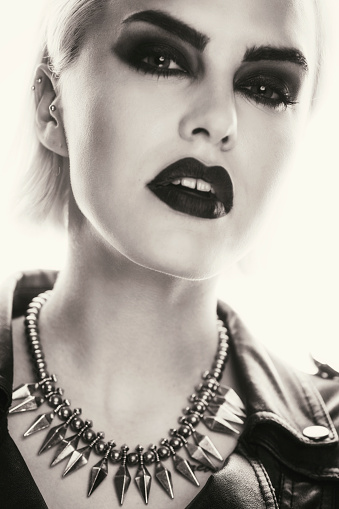 Black and white portrait of a beautiful blonde woman with a black smokey eyes make-up and black lips, wearing black ramones leather jacket.