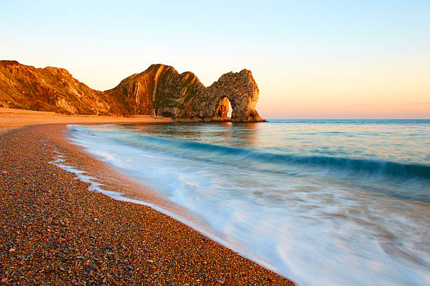 Durdle Door On Dorset's Jurassic Coast Looking across a shingle beach towards the magnificent natural arch that is Durdle Door on Dorset's Jurassic Coast. durdle door stock pictures, royalty-free photos & images