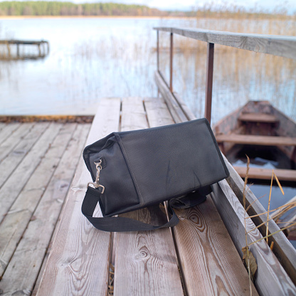 Forgotten black bag on a pier, lake and boat on the blurred background