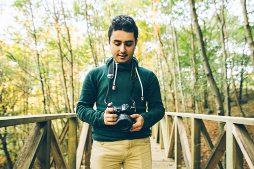 A young man holding a DLSR camera in a natural environment.