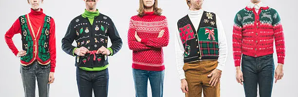 A panoramic image of a large group of people wearing knit ugly Christmas sweaters and cardigans with various bizarre patterns and decorations.  Horizontal on white studio background.