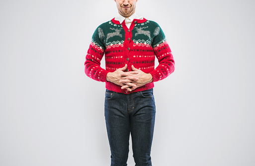 A young man in a Christmas sweater smiles proudly, showing of his clothing.  Cropped at top of face, emphasis on the sweater.  White studio background with copy space.