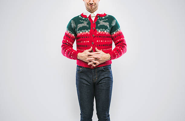 Christmas Sweater Man A young man in a Christmas sweater smiles proudly, showing of his clothing.  Cropped at top of face, emphasis on the sweater.  White studio background with copy space. christmas ugliness sweater nerd stock pictures, royalty-free photos & images