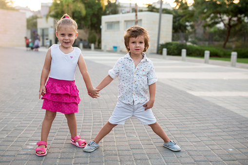 Cute girl and boy standing on the street while holding hands and looking at the camera.