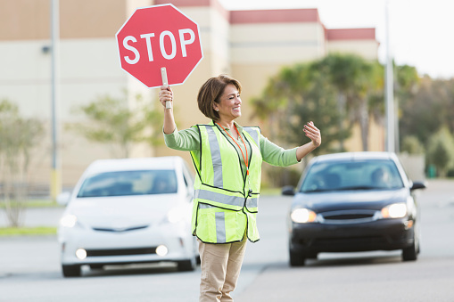 Hispanic woman (50s) with stop sign directing traffic.