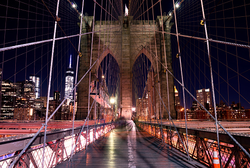 Night at Brooklyn bridge with illuminating buildings from Manhattan in background. New York City, US.