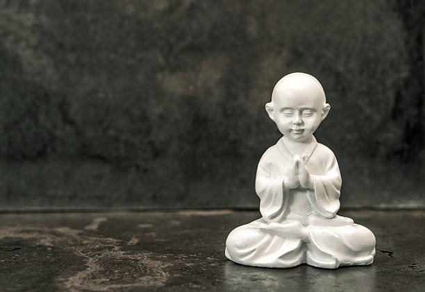 Buddha statue on dark background. Praying white monk. Meditation concept.  Vintage style toned picture