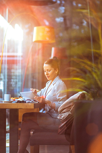 Young, trendy businesswoman using her digital tablet at a restaurant. Long dark hair tied in a bun, formalwear.