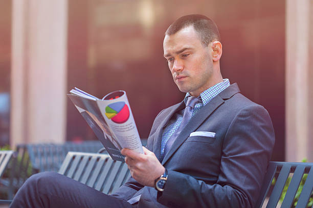 Businessman reading magazine outdoors stock photo