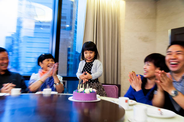 Asian family celebrating a birthday, candels have just been blown out. Focus on girl, lots of blurred motion.