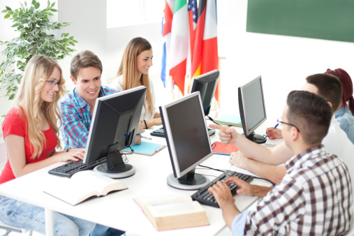 Happy teenage girl communicating with professor who is using computer during a class in the classroom.