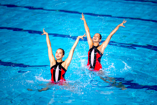 Synchronized swimming competion. Two beautiful girls performing in the swimming pool