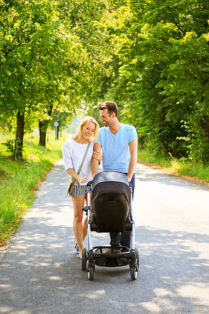 Outdoor portrait of happy couple walking with baby stroller in a park.