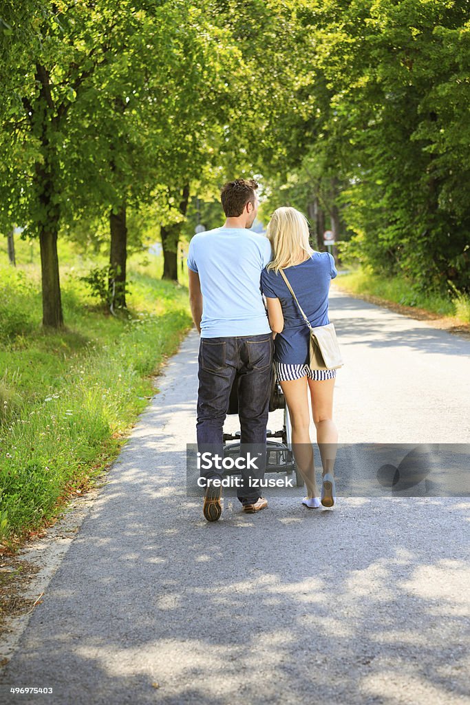 Couple walking in a park Back view of couple walking with baby stroller in a park. Adult Stock Photo