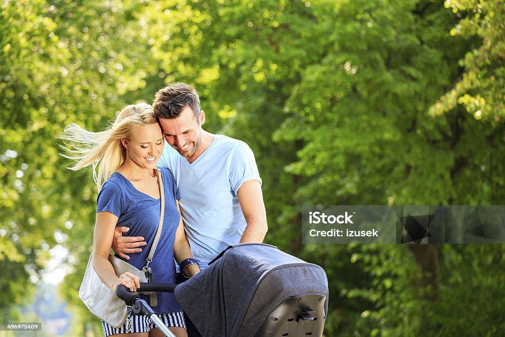 Happy couple in a park Outdoor portrait of happy couple walking with baby stroller in a park. Adult Stock Photo