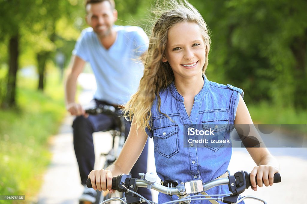 Happy girl cycling Outdoor portrait of happy girl cycling on a bicycles in a park with her father. Focus on the girl smiling at the camera. Summer Stock Photo