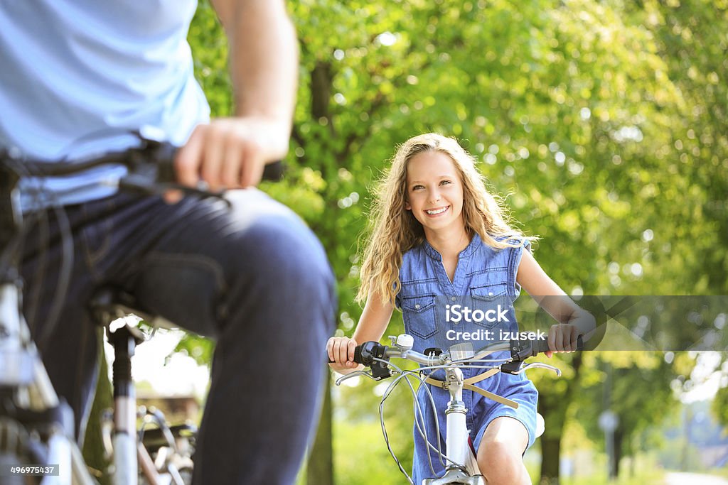Happy girl cycling Outdoor portrait of happy girl cycling on a bicycles in a park with her father. Focus on the girl. Family Stock Photo