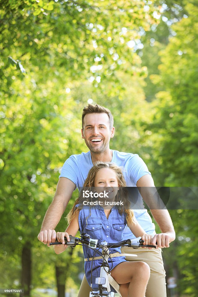 Father cycling with his daughter Outdoor portrait of happy father and daughter cycling on a bike together, smiling at the camera. Bicycle Stock Photo