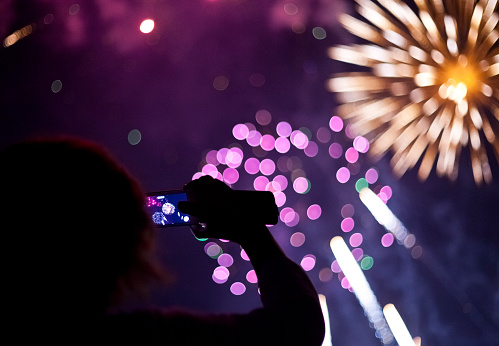 Silhouetted person photographing a colorful Fireworks with a smartphone