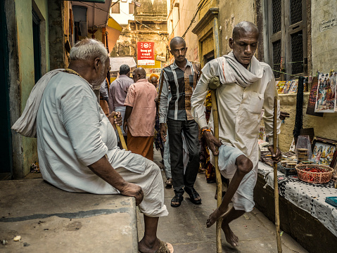 Varanasi, India - October 05, 2015: People walking in the narrow alleys of Varanasi. In the past Poliomyelitis was very spread in India causing thousands of deformities specially in the legs. Since January 2011, there have been no reported cases of the wild polio infections in India . This is one of the oldest inhabited cities in the world and also the holiest of the seven sacred cities in Hinduism and Jainism and so the most important pilgrimage place for hindus. 