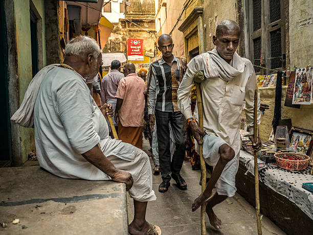 Varanasi India Varanasi, India - October 05, 2015: People walking in the narrow alleys of Varanasi. In the past Poliomyelitis was very spread in India causing thousands of deformities specially in the legs. Since January 2011, there have been no reported cases of the wild polio infections in India . This is one of the oldest inhabited cities in the world and also the holiest of the seven sacred cities in Hinduism and Jainism and so the most important pilgrimage place for hindus.  polio virus photos stock pictures, royalty-free photos & images