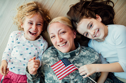 Military mom lying on floor with her two children, little girls. Looking at camera and smiling. Having some happy time together. Mother just return from some of army missions. Shot with Canon EOS 5Ds 50mp