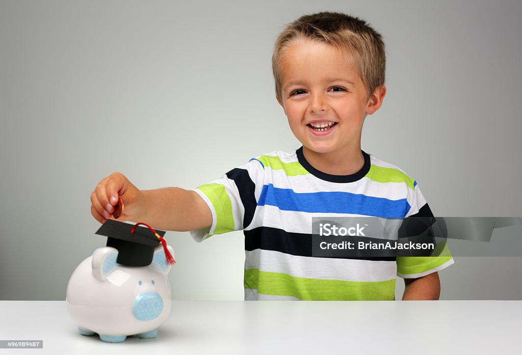 Saving for an education Young boy putting money into a piggy bank with a graduation mortar board cap concept for the cost of a college education Allowance Stock Photo