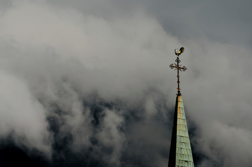Church steeple with a cross and weathervane and stormy background