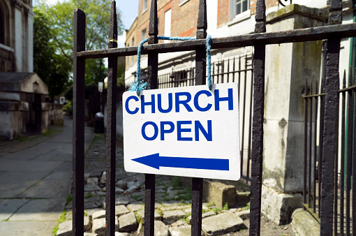 A sign on a church gate advising passersby that the church is open for worship or for sightseeing. The church is St Alfege at Greenwich in South East London, designed by Nicholas Hawksmoor and begun in 1712 to replace the earlier building which had collapsed in a storm in 1710.